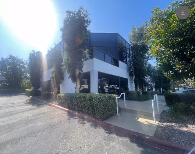 Exterior view of Manor Hospice building with glass facade, trees, and accessible entrance ramp.