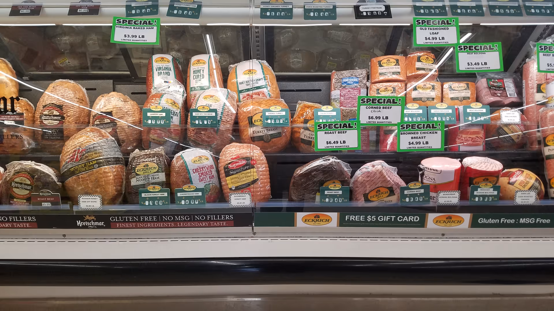 Glass refrigerated display case filled with assorted cheeses and cured meats.