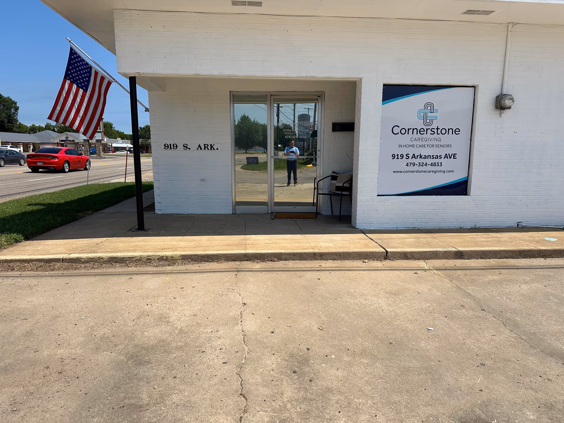 White brick building entrance with Cornerstone Caregiving banner and US flag outside.
