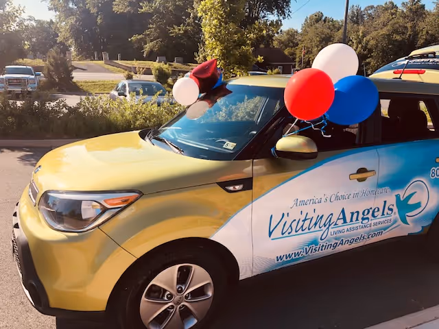 Decorated Visiting Angels van with balloons parked in a sunny outdoor lot.