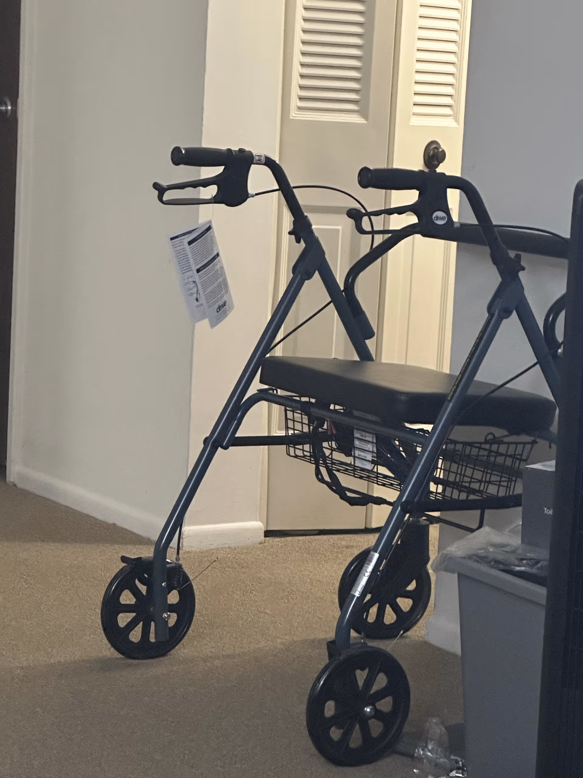 A black rollator walker sits in a hallway near closet doors.