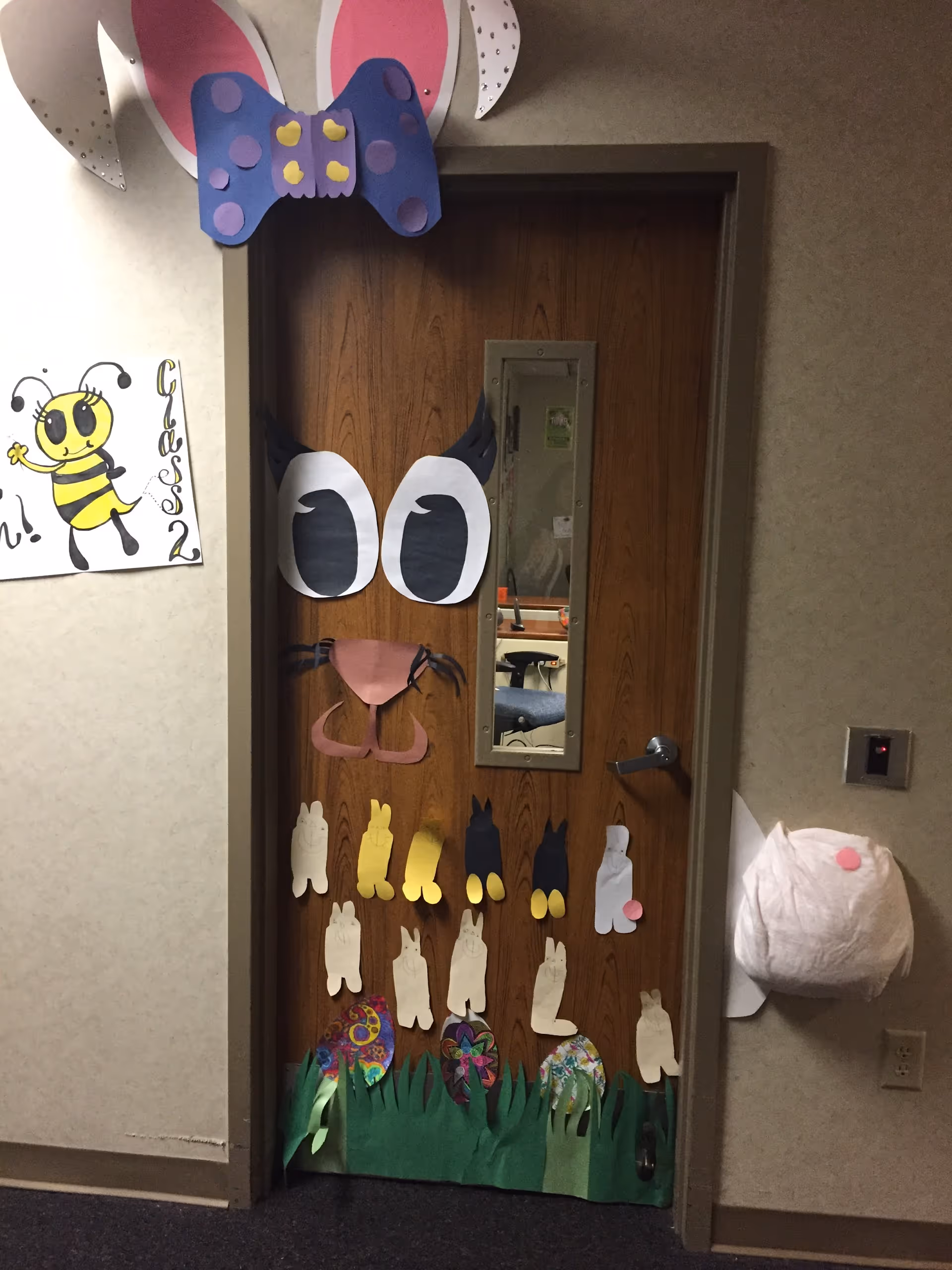Door decorated with cartoon animal cutouts and grass in a hallway.