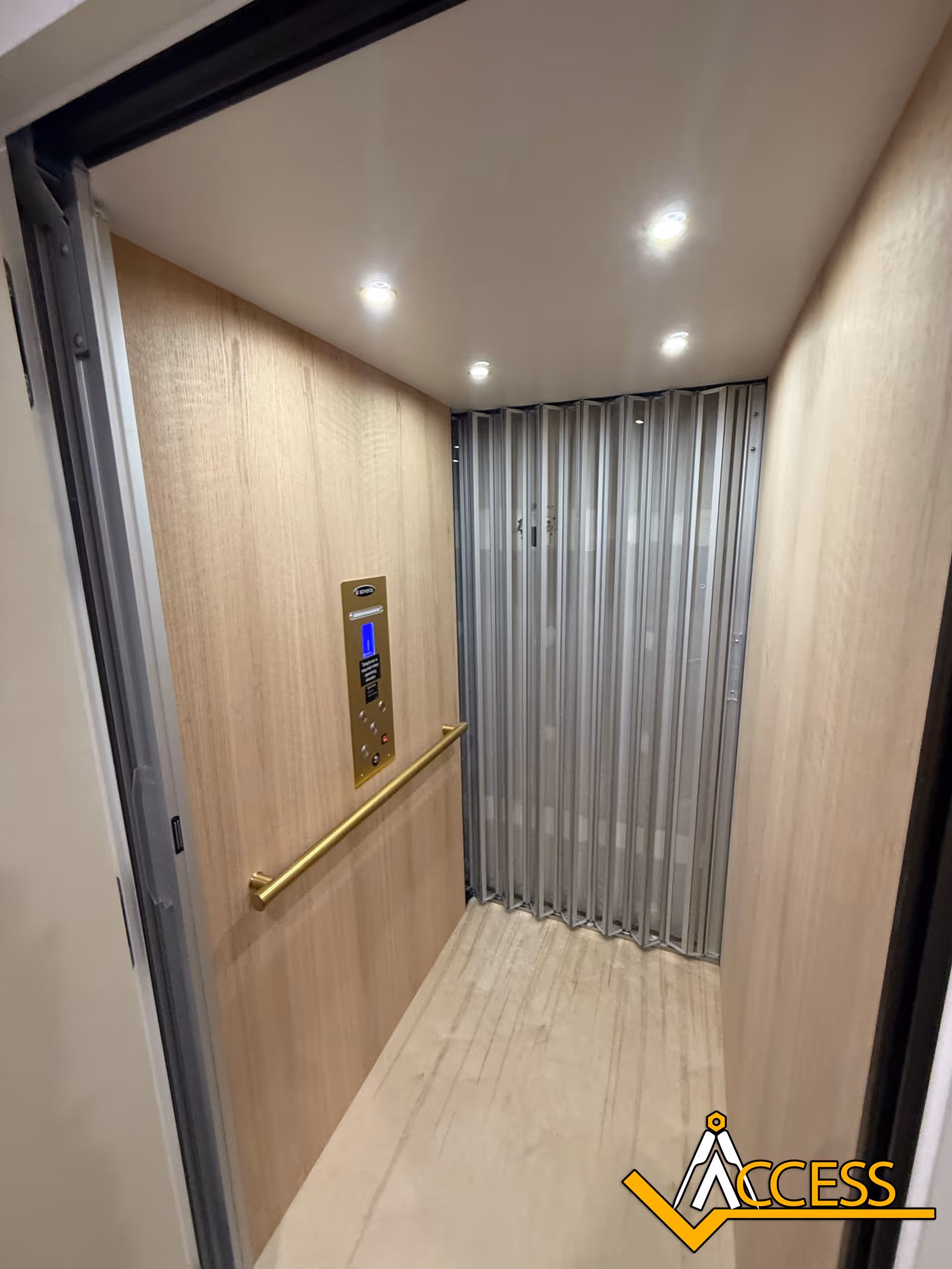 Elevator cab interior with wood panels, lit ceiling, control panel, and railing.