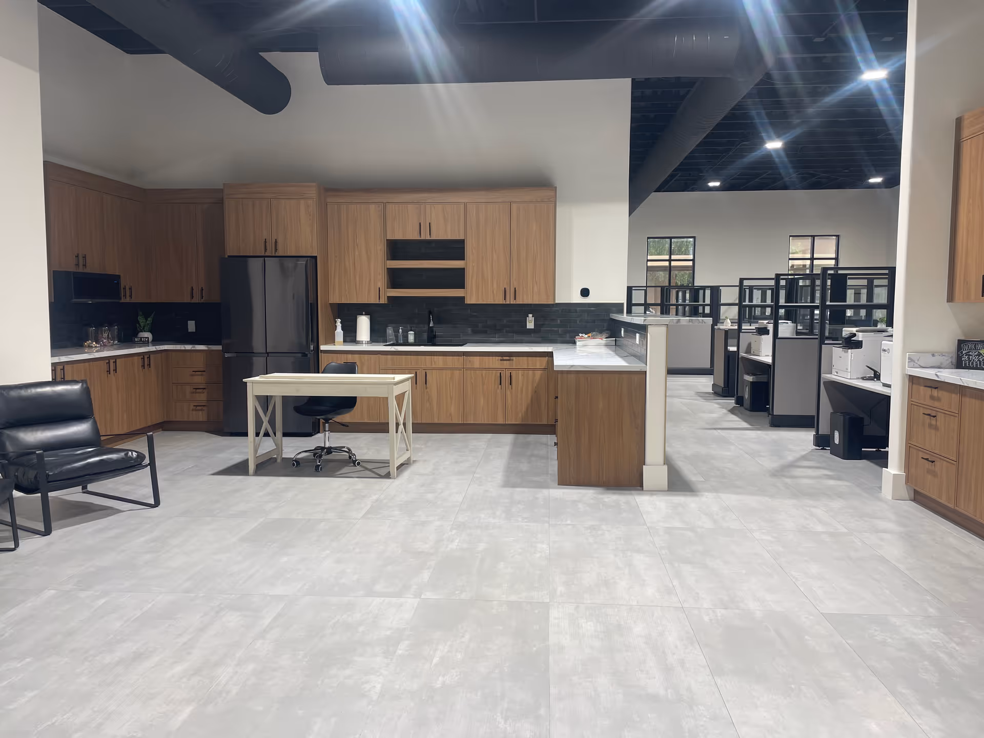 Open kitchen area with wooden cabinets, appliances, and a small central table in a bright facility.