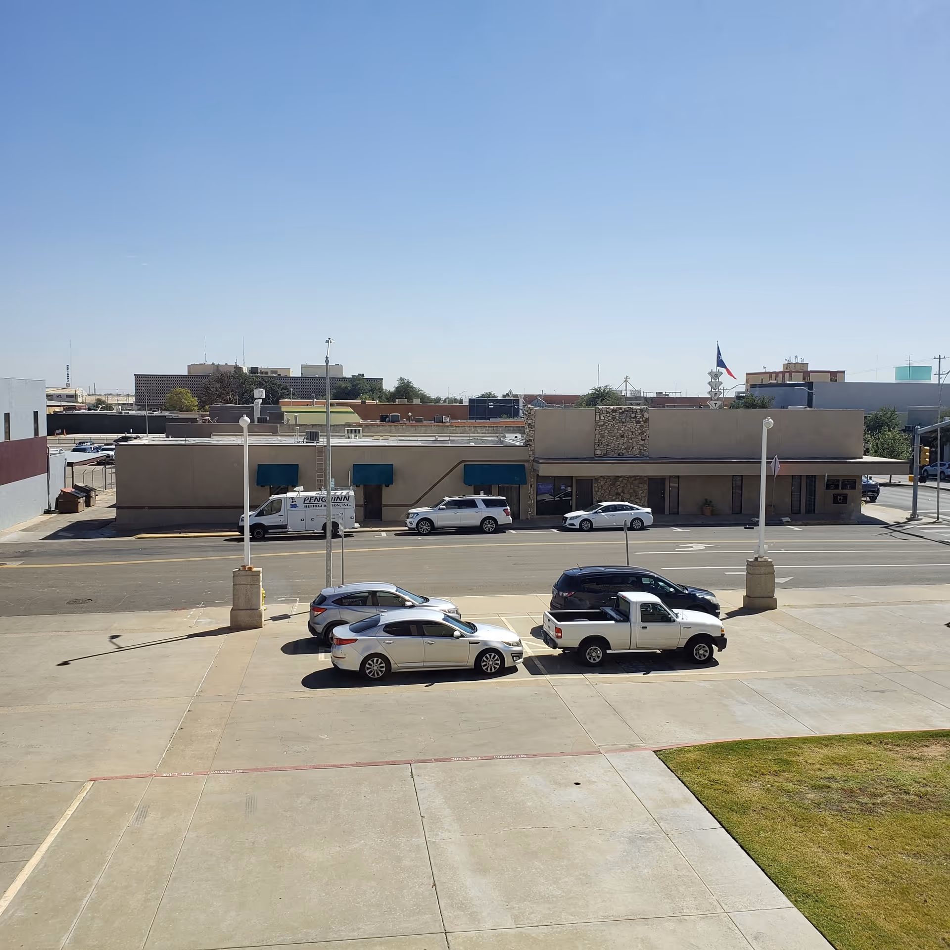 Street view of a single-story building with blue awnings and parked cars.