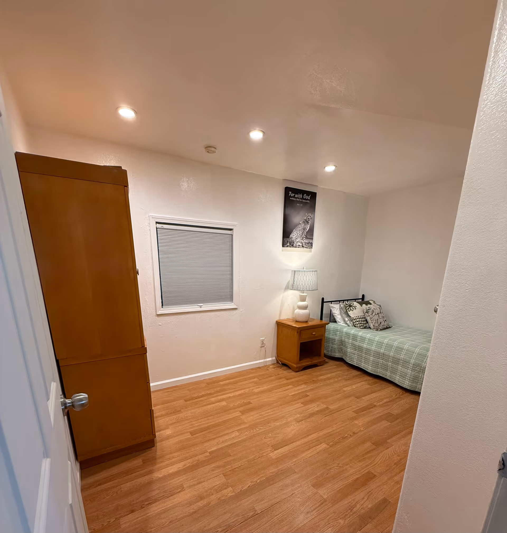 Simple bedroom in a senior care facility with bed, nightstand, and wardrobe.