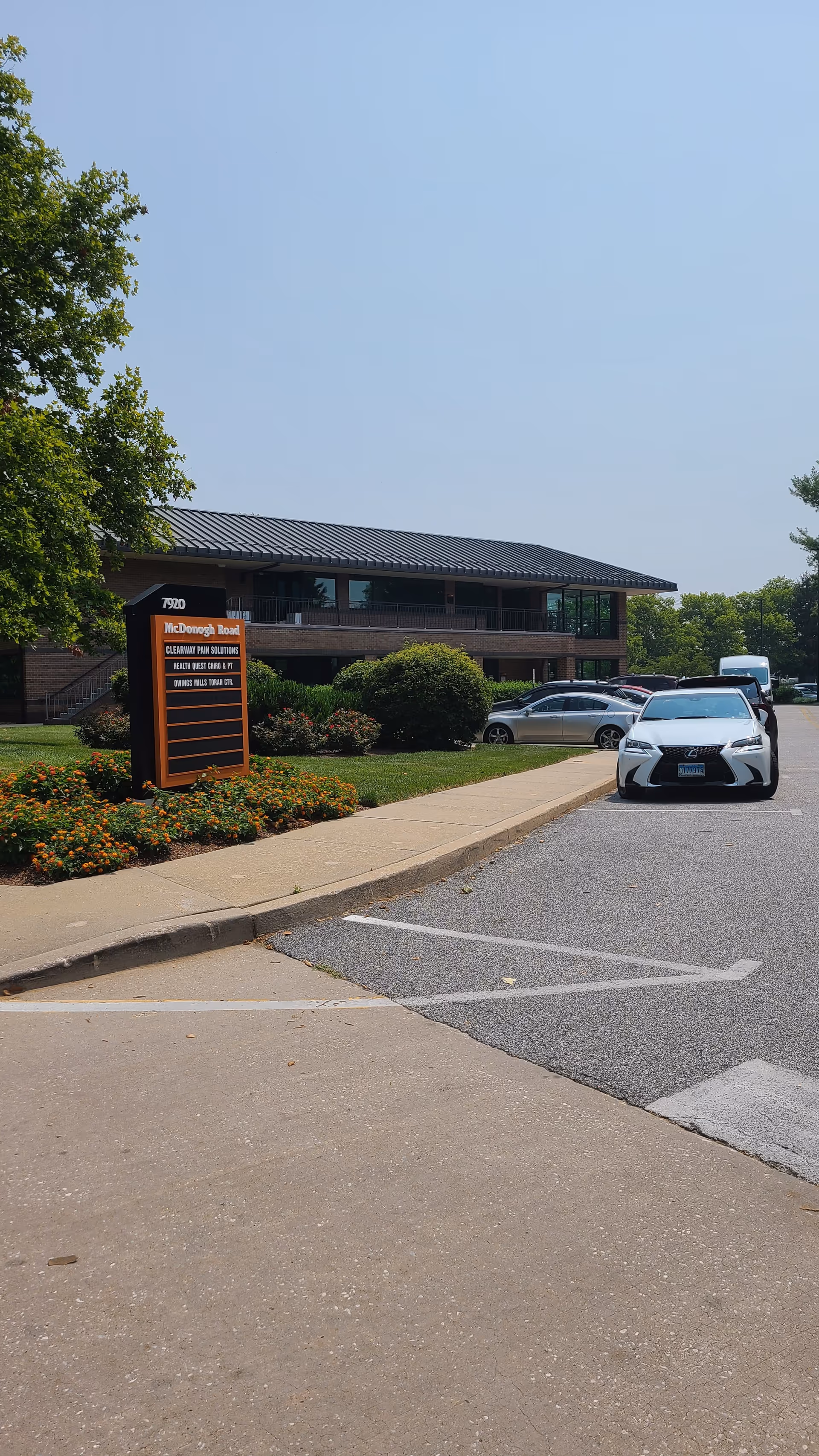 Brick, two-story facility building with a parking lot and landscaped entrance under a clear blue sky.