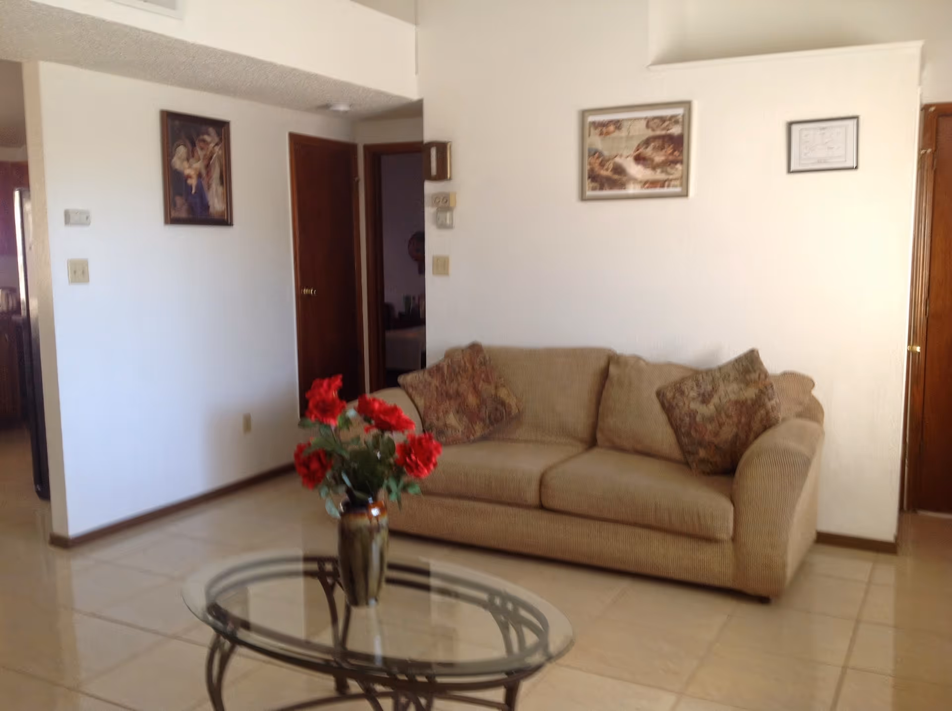 Beige sofa with a red flower vase and glass coffee table in a bright living room.