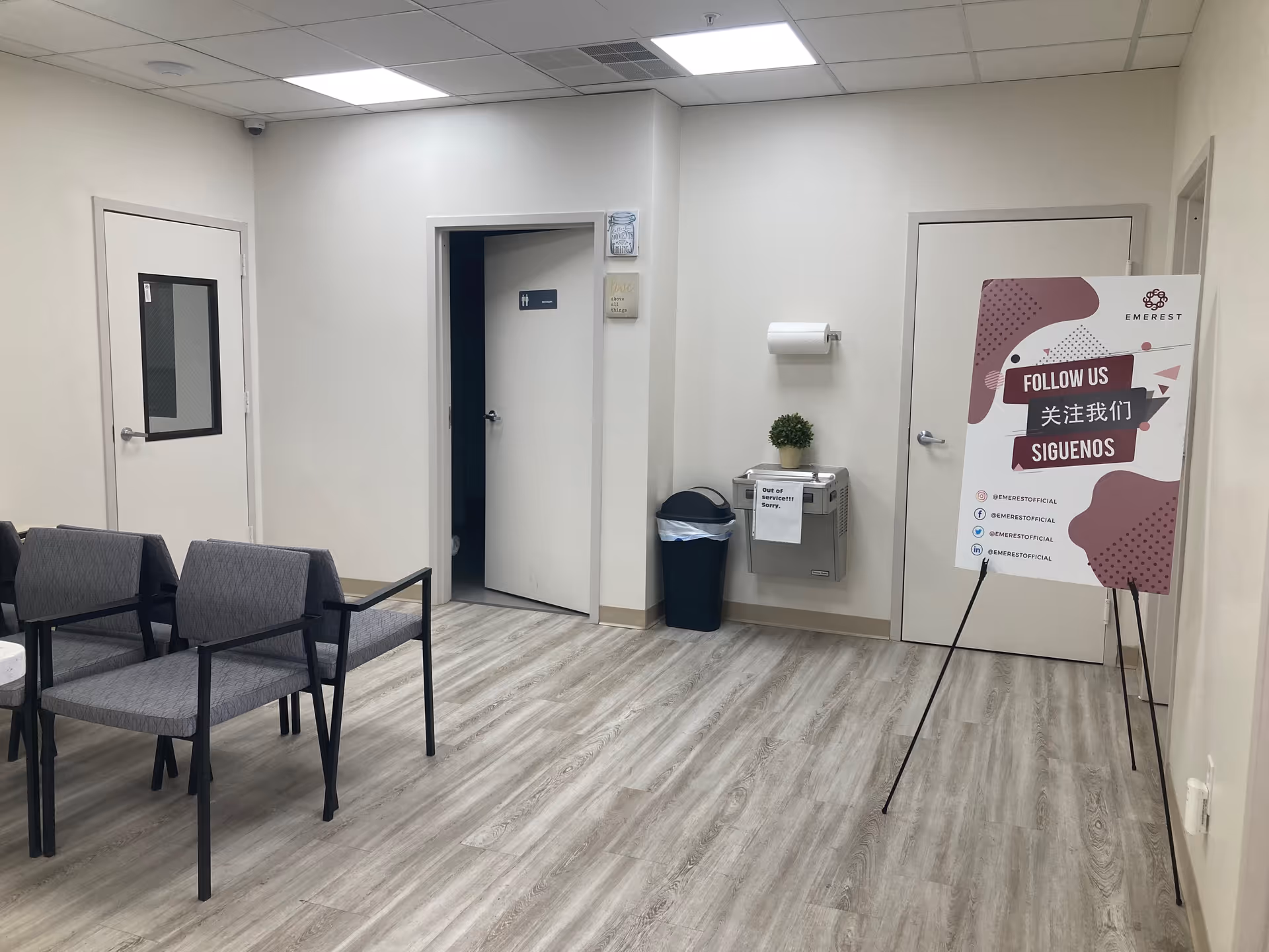 Interior waiting area with gray chairs, doors, a trash bin, and a promotional sign.