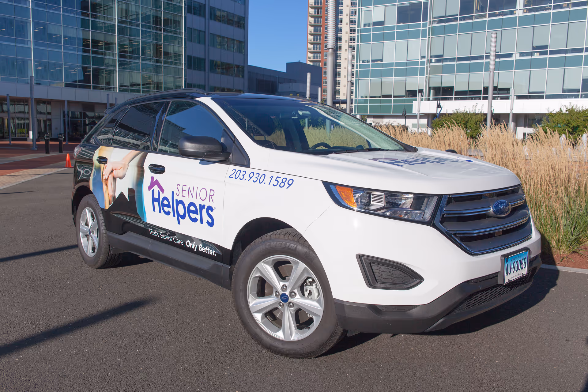 White Senior Helpers branded SUV parked in front of a modern glass office building.