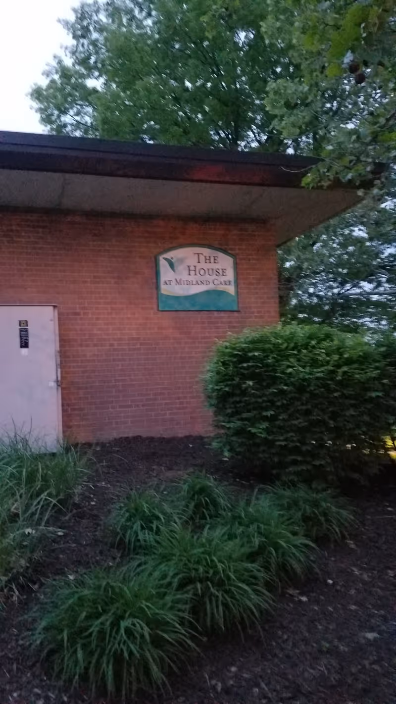 Brick exterior of Midland Care building with sign and surrounding shrubs and trees