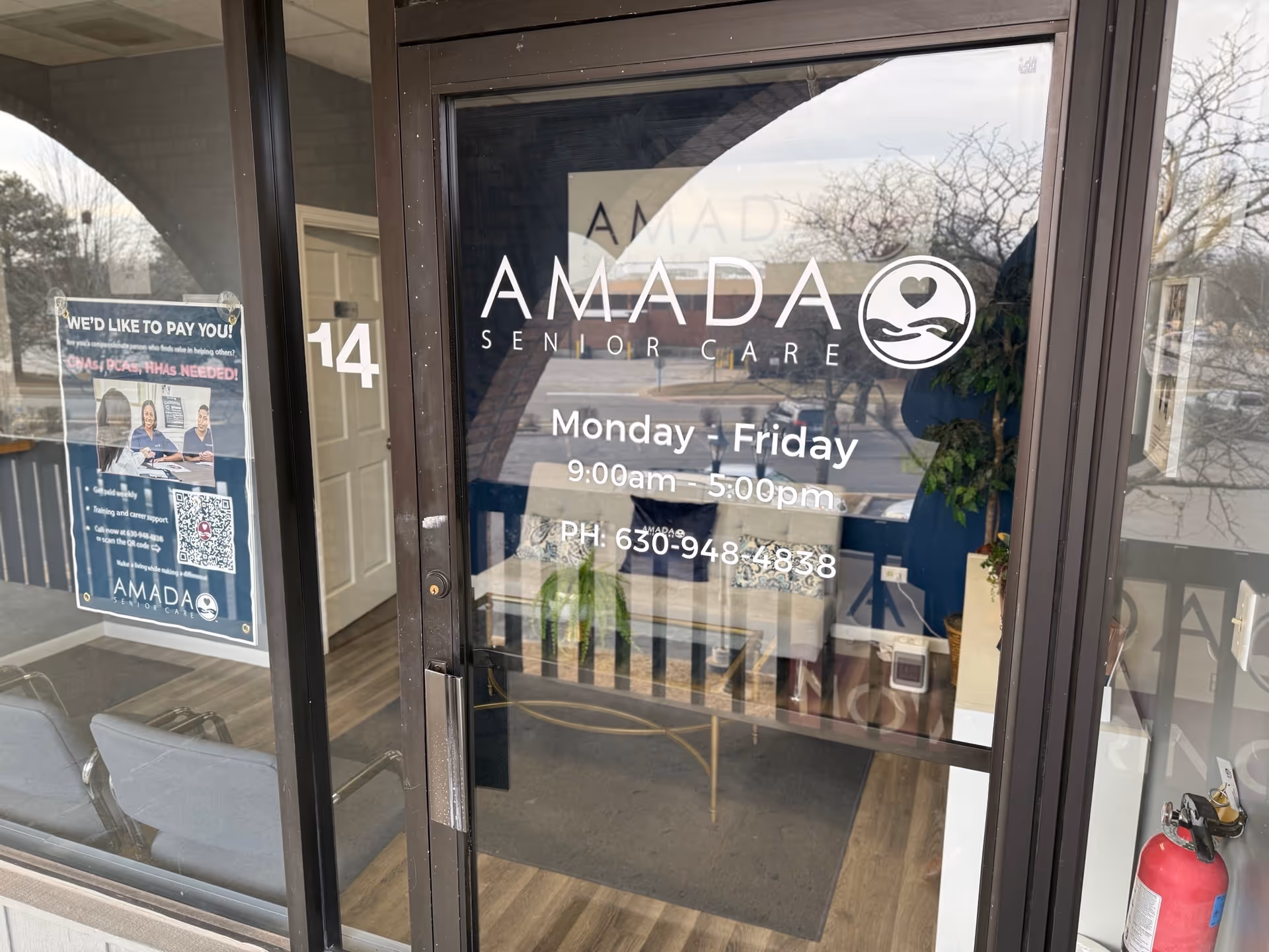 Glass entrance door with Amada Senior Care logo and hours, interior seating visible.