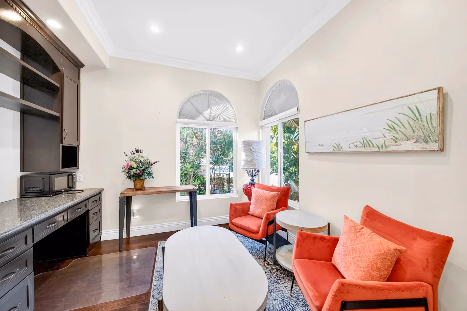 Cozy senior living lounge with red chairs, coffee table, and kitchenette along the wall.