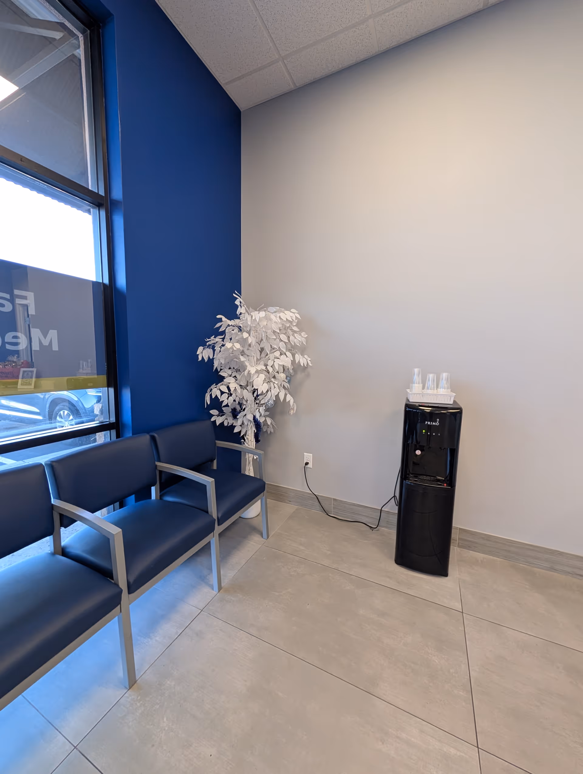 Interior waiting area with blue chairs, a water cooler, and a white plant.