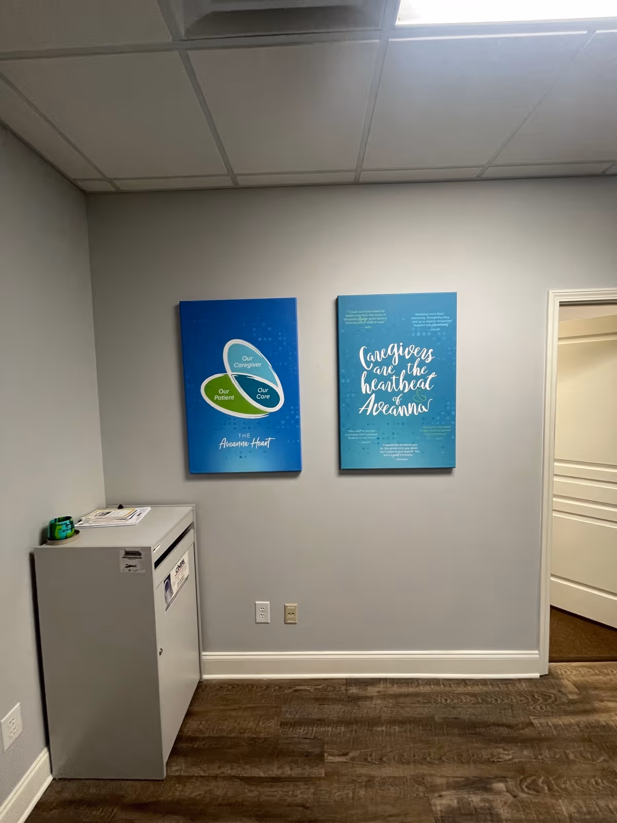 Hallway interior at Aveanna Hospice of Cullman with blue posters and a small cabinet.
