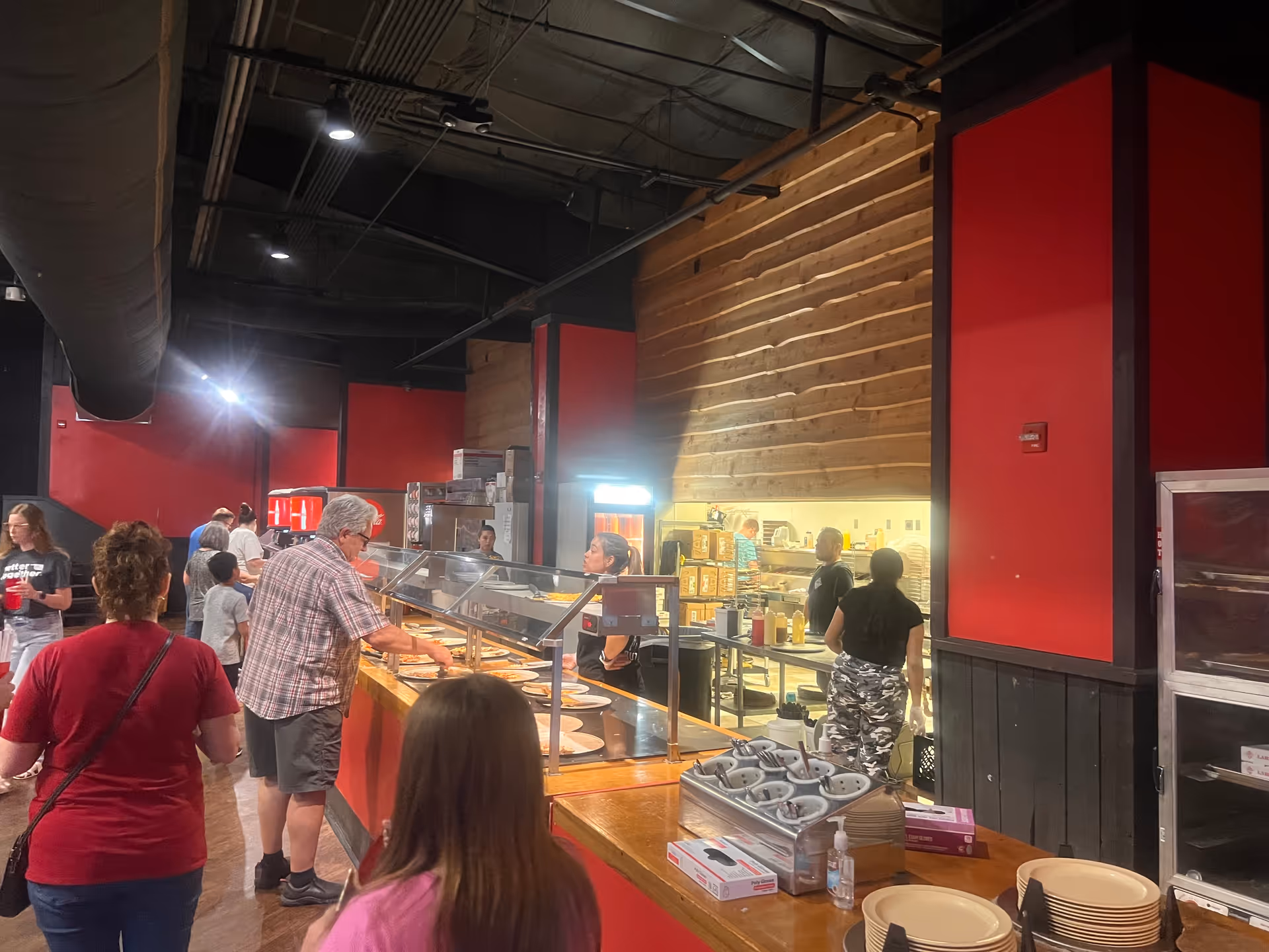 Residents line up at a cafeteria-style serving line inside a red-walled dining area.