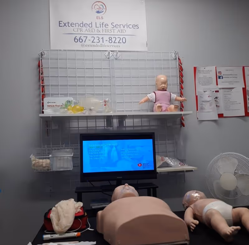 Interior CPR training station with mannequins, monitor, and medical supplies on shelves.