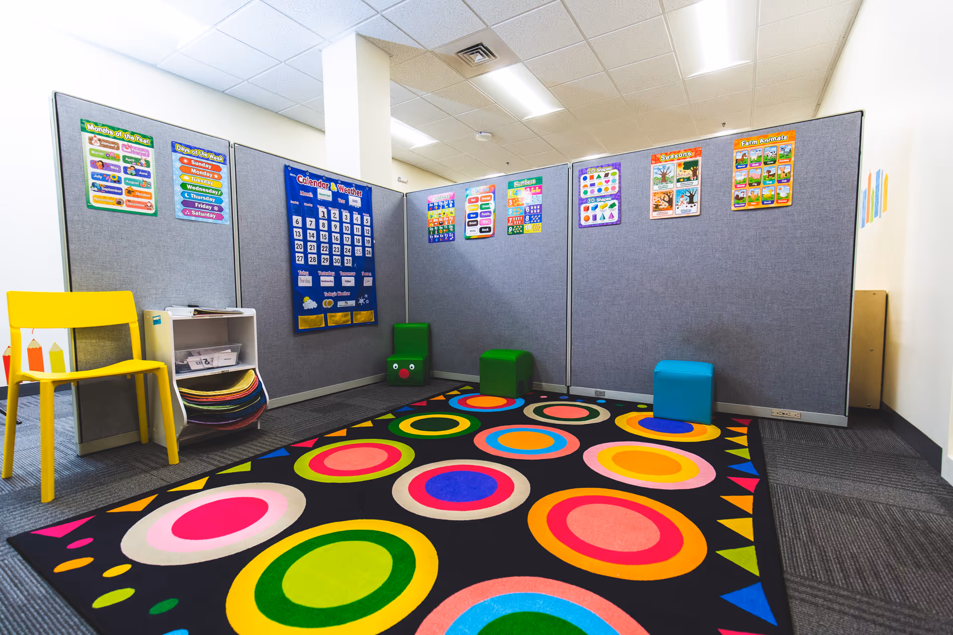 Colorful activity room with bright circular rug, posters, and a yellow chair.