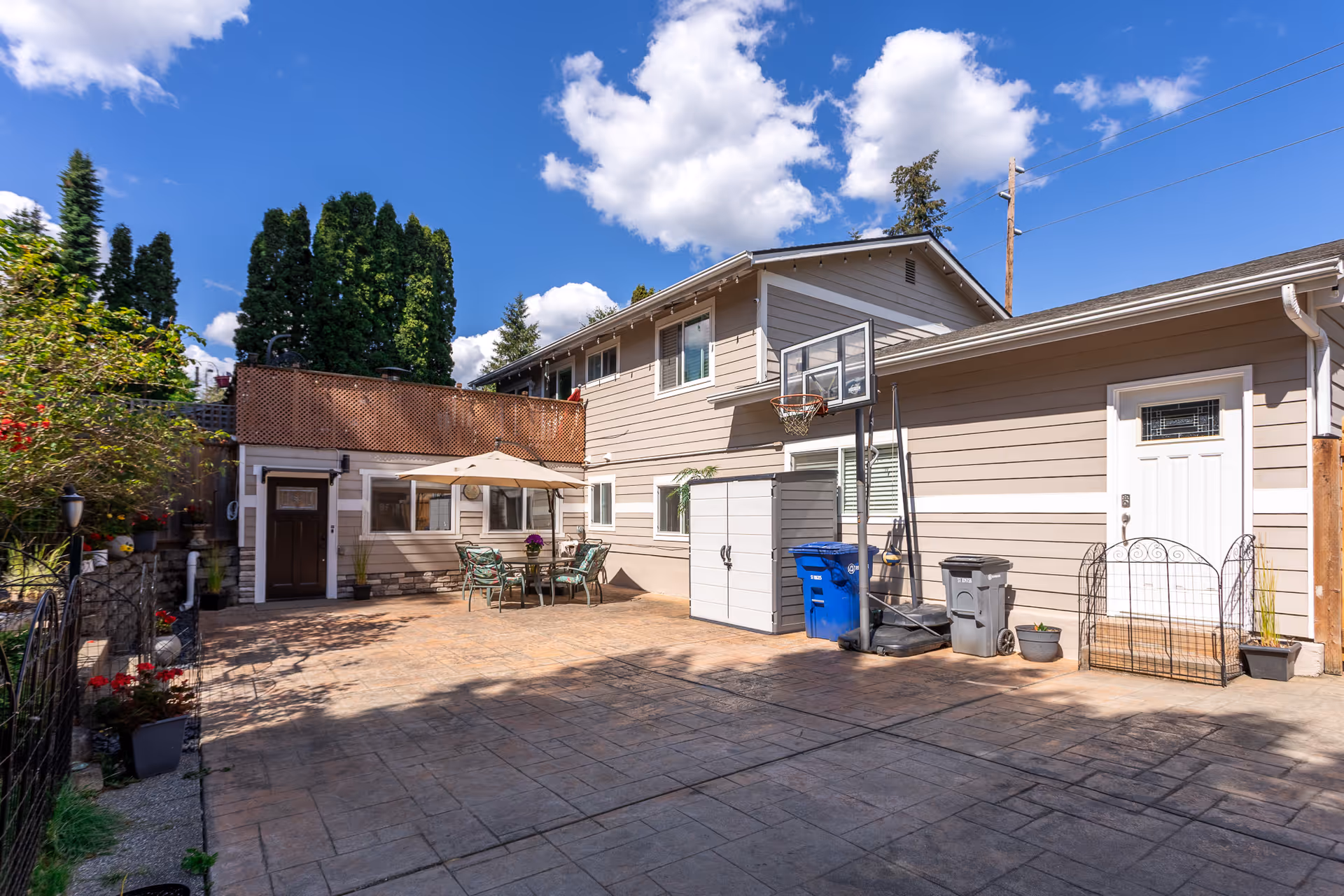 Residential building exterior with patio, outdoor seating, basketball hoop, and storage shed.