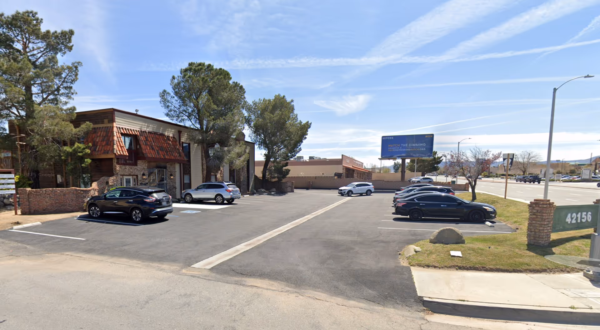 Parking lot in front of a rustic building with trees under a blue sky.
