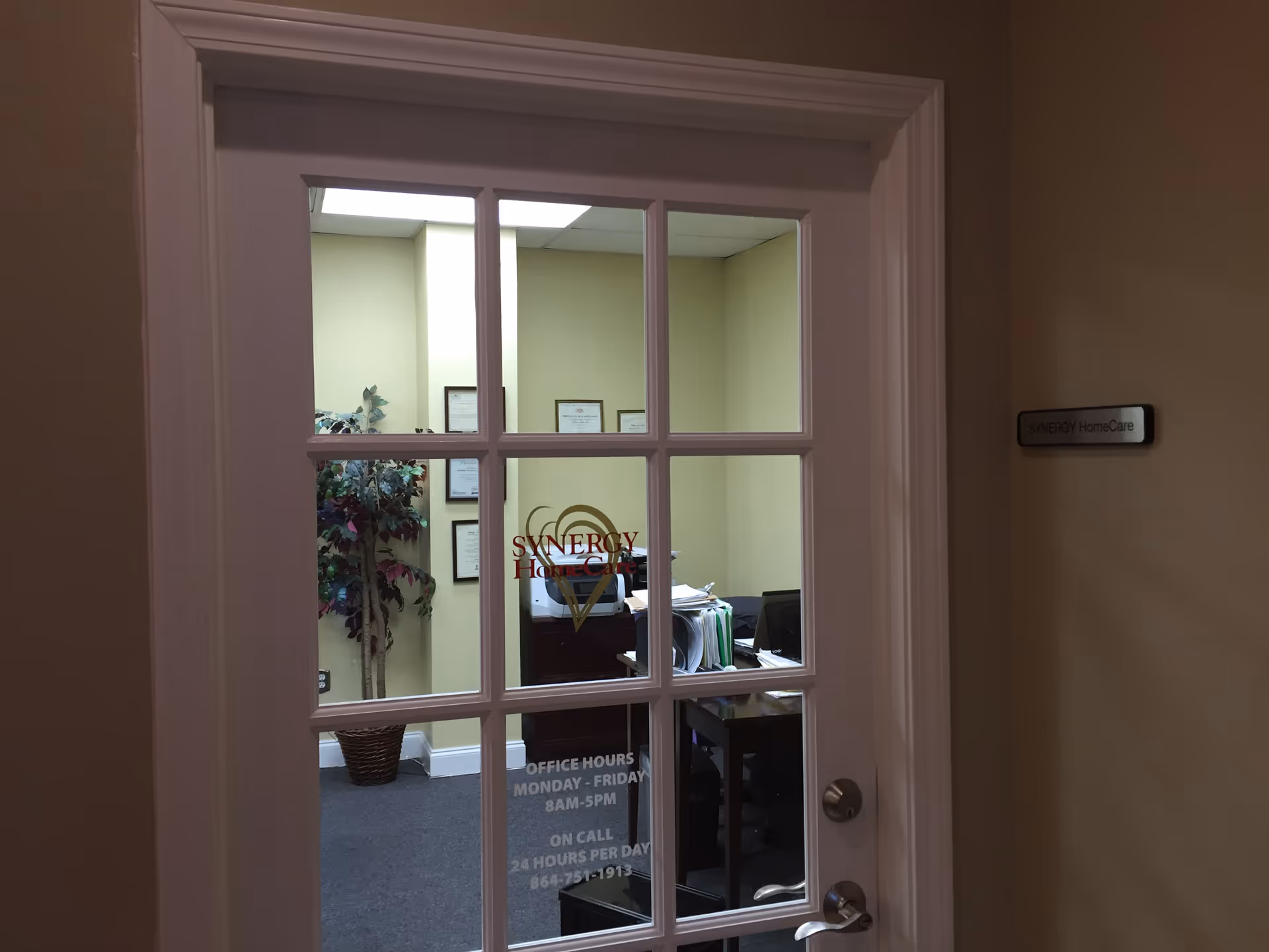 Glass-paned door opens to a reception office with framed certificates and a plant.