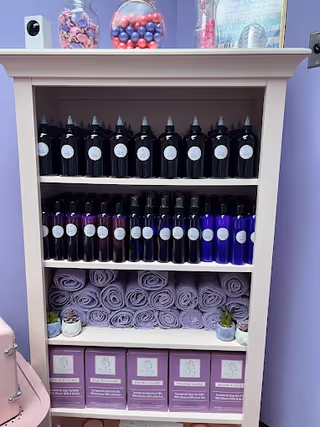 Shelf unit in a salon interior with dark bottles, purple towels, lavender decor.