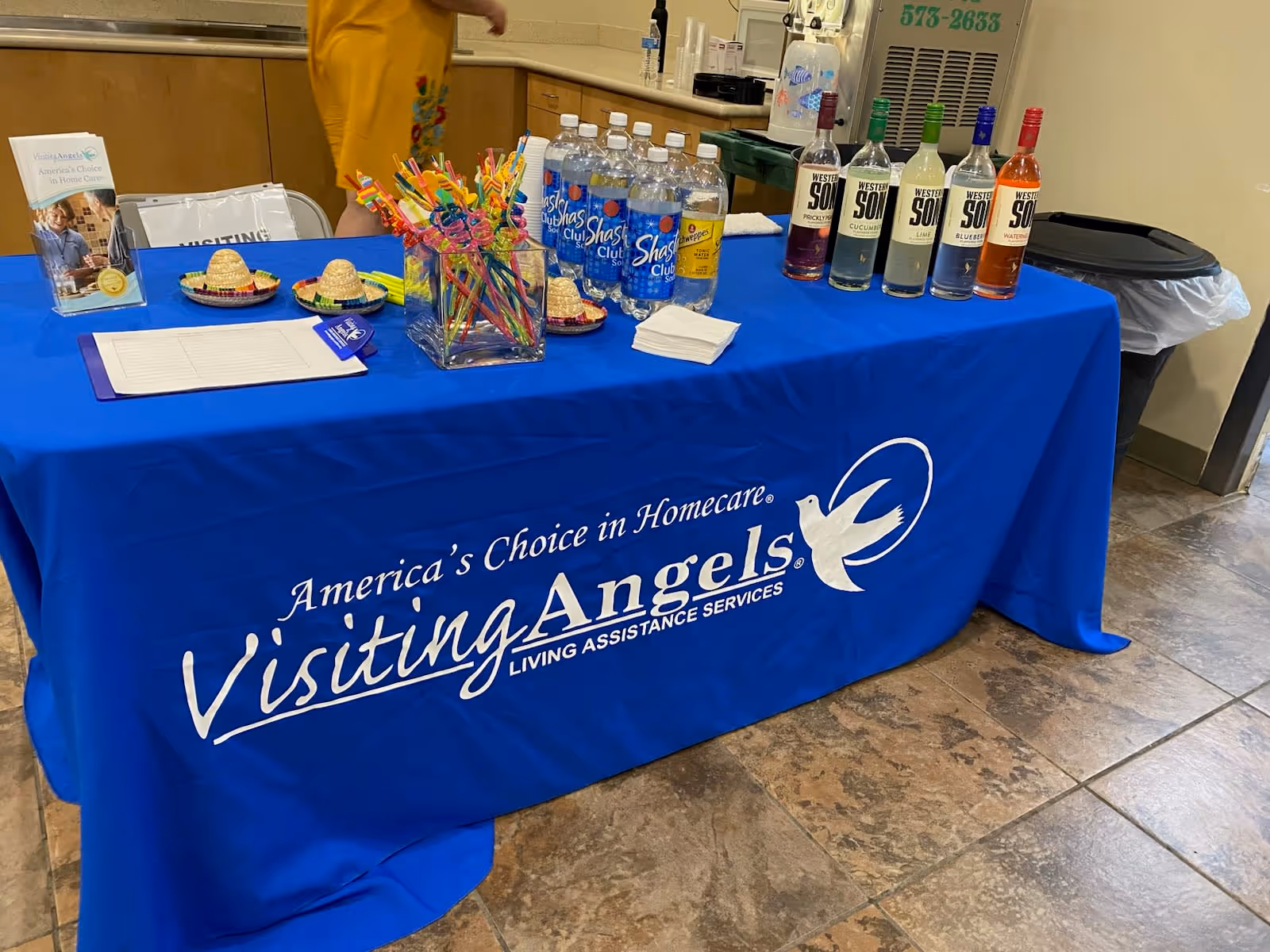 Blue Visiting Angels table with beverages and signage in a facility lobby.