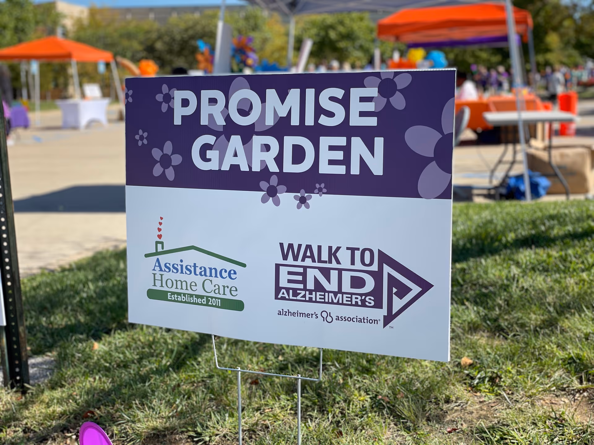 Purple sign reads Promise Garden at an outdoor event for Assistance Home Care and Alzheimer's awareness.