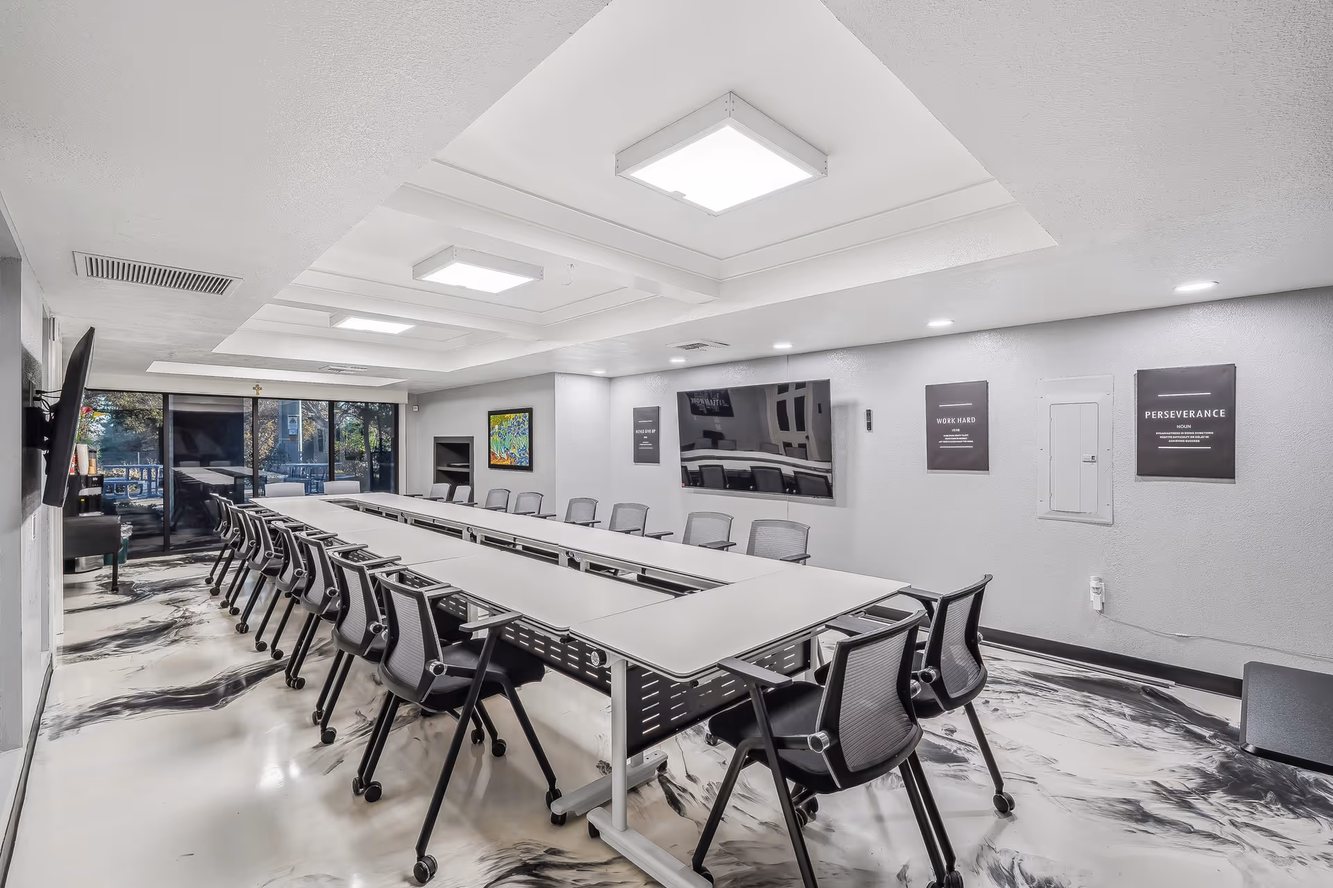 A modern conference room with a long U-shaped table, chairs, and a large wall screen.