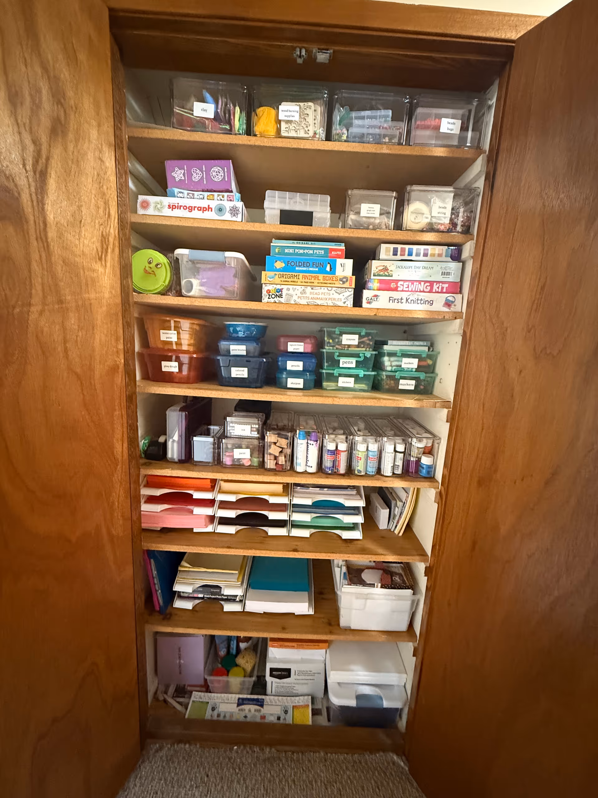 Tall wooden cabinet with shelves holding craft supplies, bins, and papers.