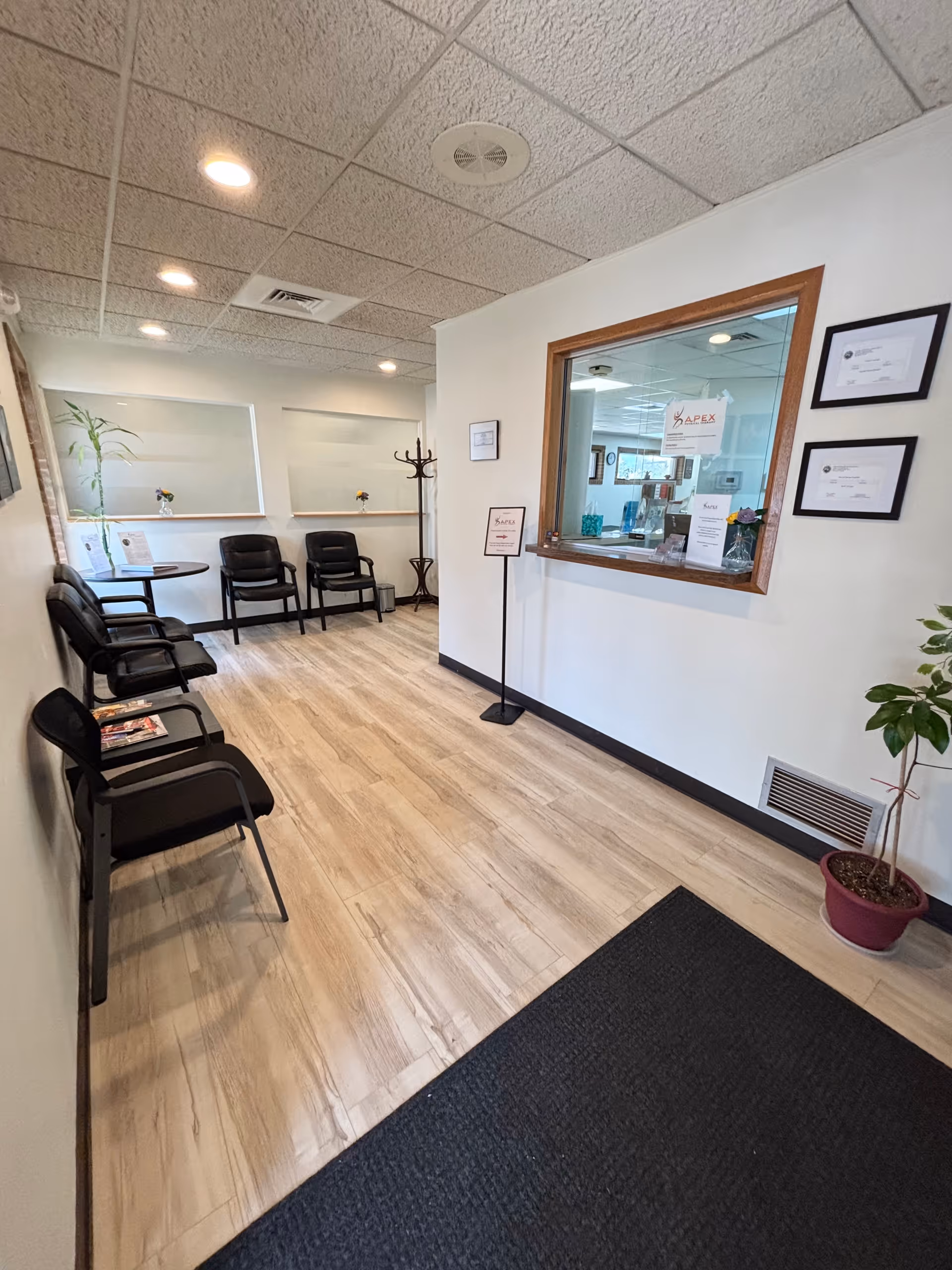 Waiting area of Apex Physical Therapy with chairs, a reception window, and framed certificates.