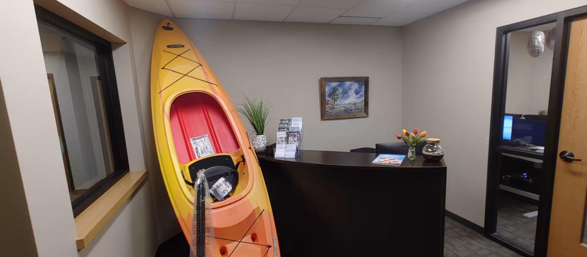Kayak stands beside a dark reception desk in a small senior care facility lobby.