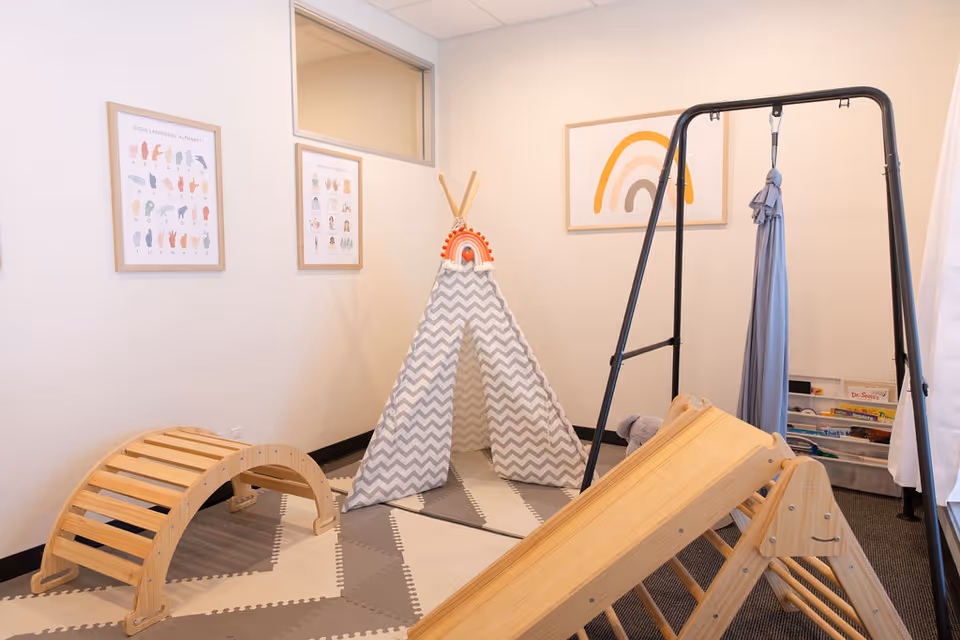 An indoor activity area with a chevron-patterned teepee, wooden climbing arches, and soft play mats.