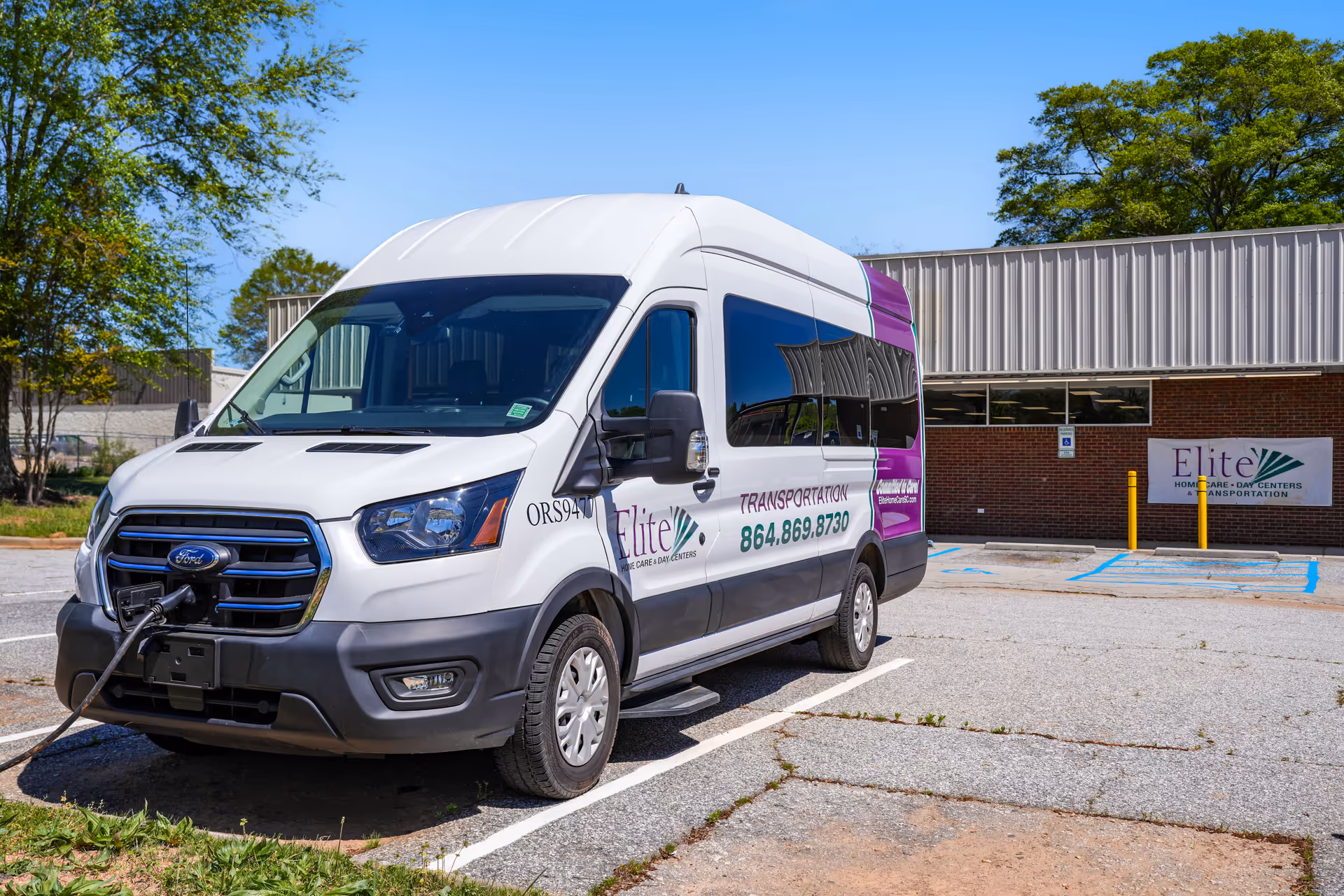 White Ford transit van with Elite Transportation branding parked outside Elite Home Care and Day Centers.