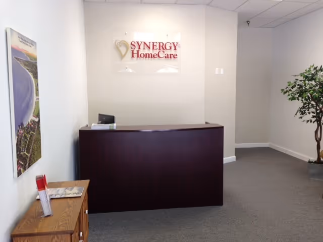 Reception desk in SYNERGY HomeCare lobby with sign, plant, and pamphlets.