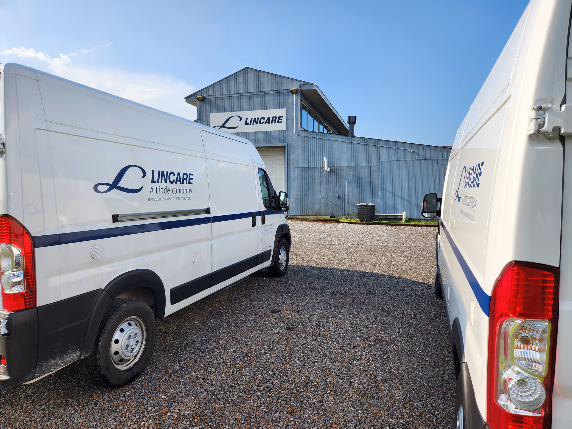 Two white LINCARE vans parked on gravel in front of a blue LINCARE building.