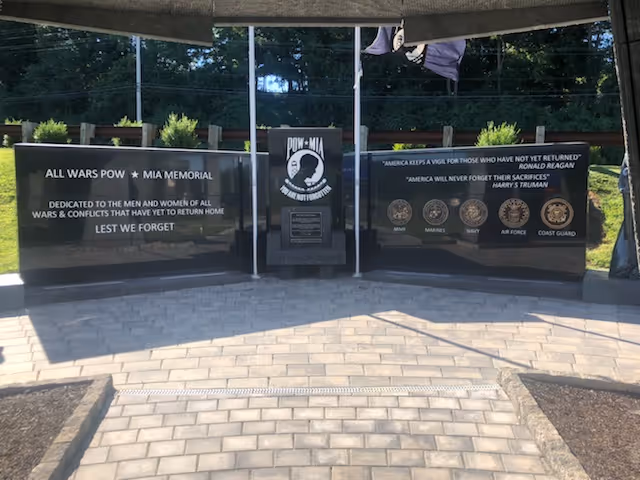 Outdoor POW-MIA memorial walls with inscriptions and central emblem along a brick walkway.