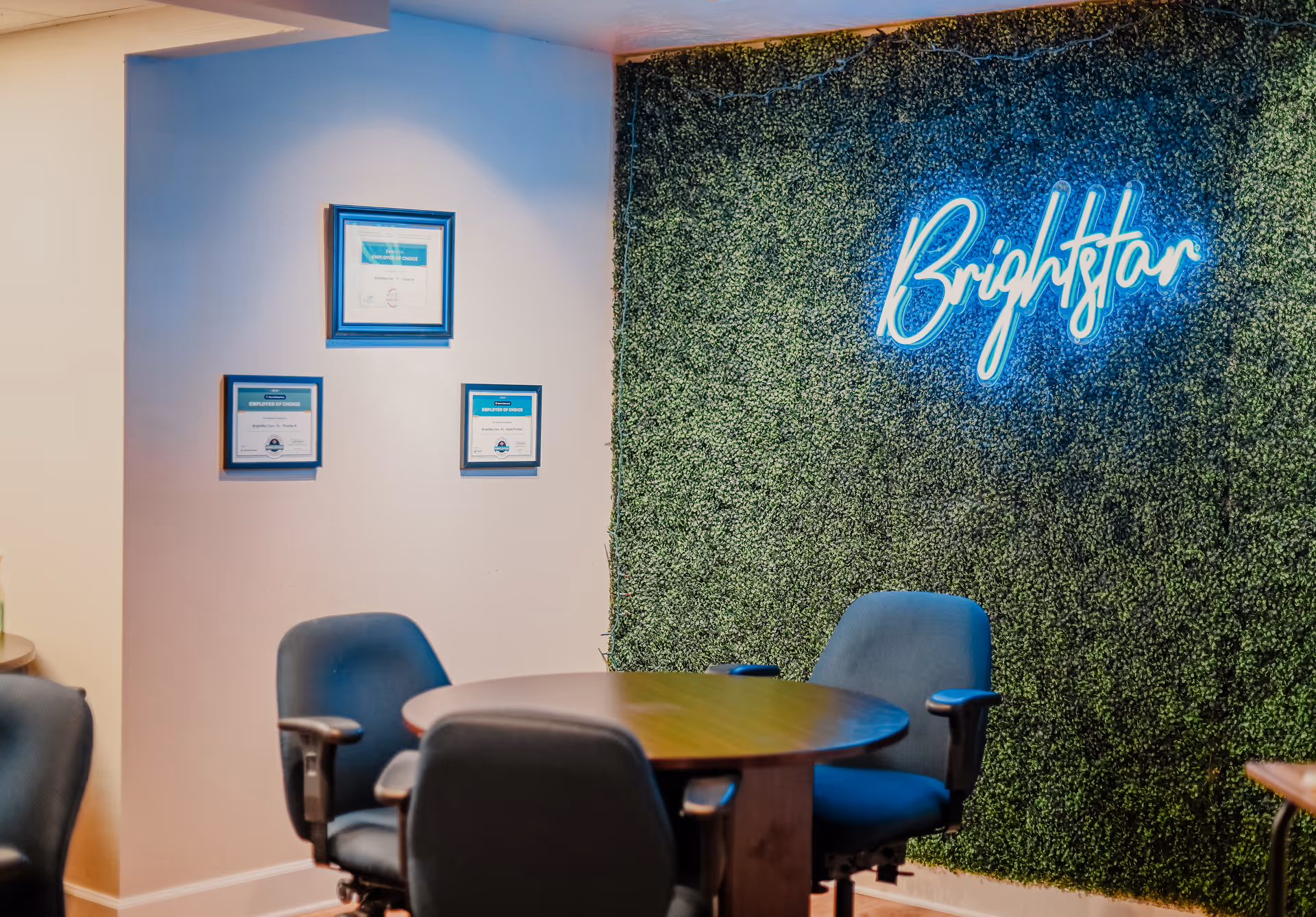 Interior reception area with round table, blue chairs, and neon BrightStar sign on a leafy wall.