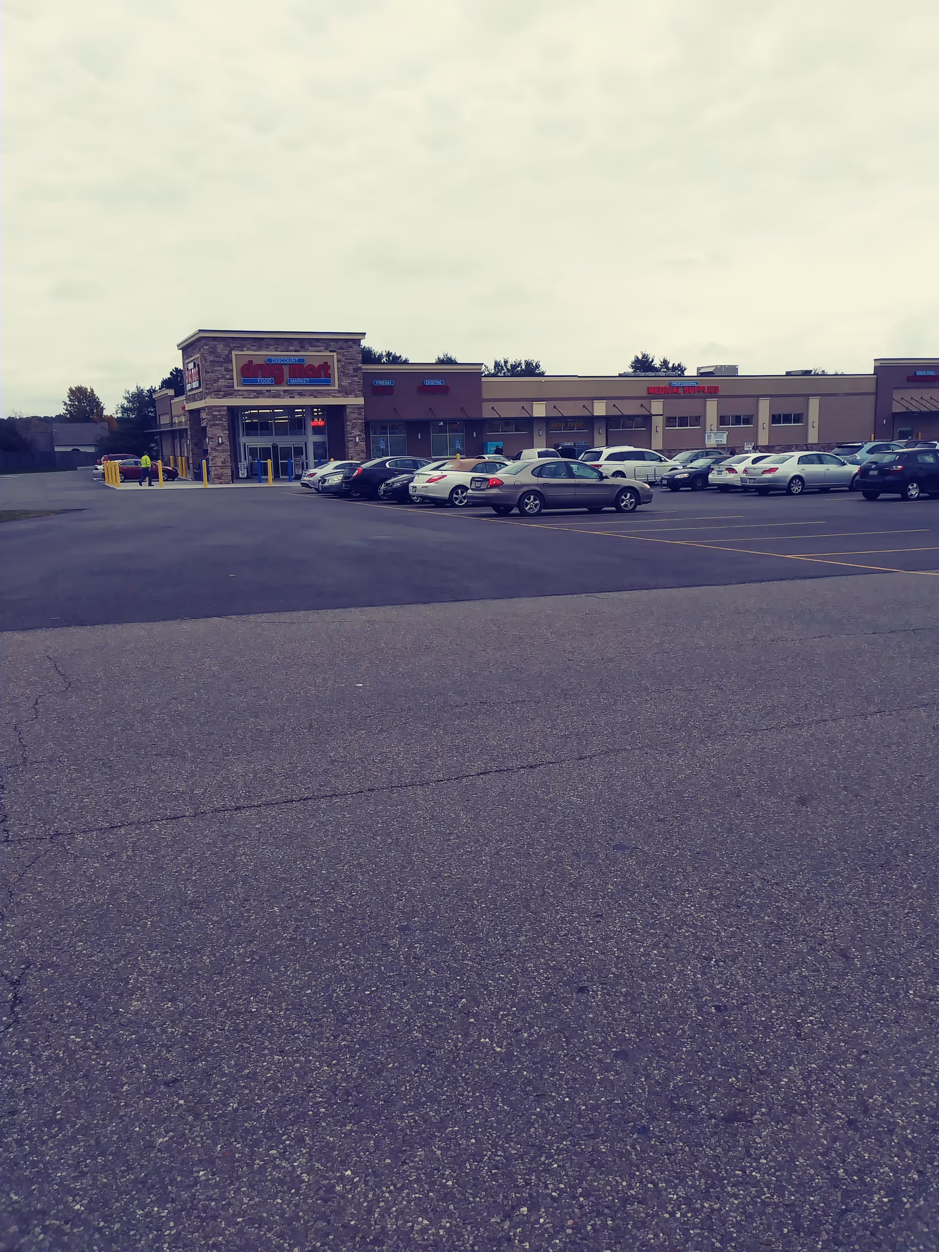 Parking lot in front of a Discount Drug Mart storefront in a strip mall.