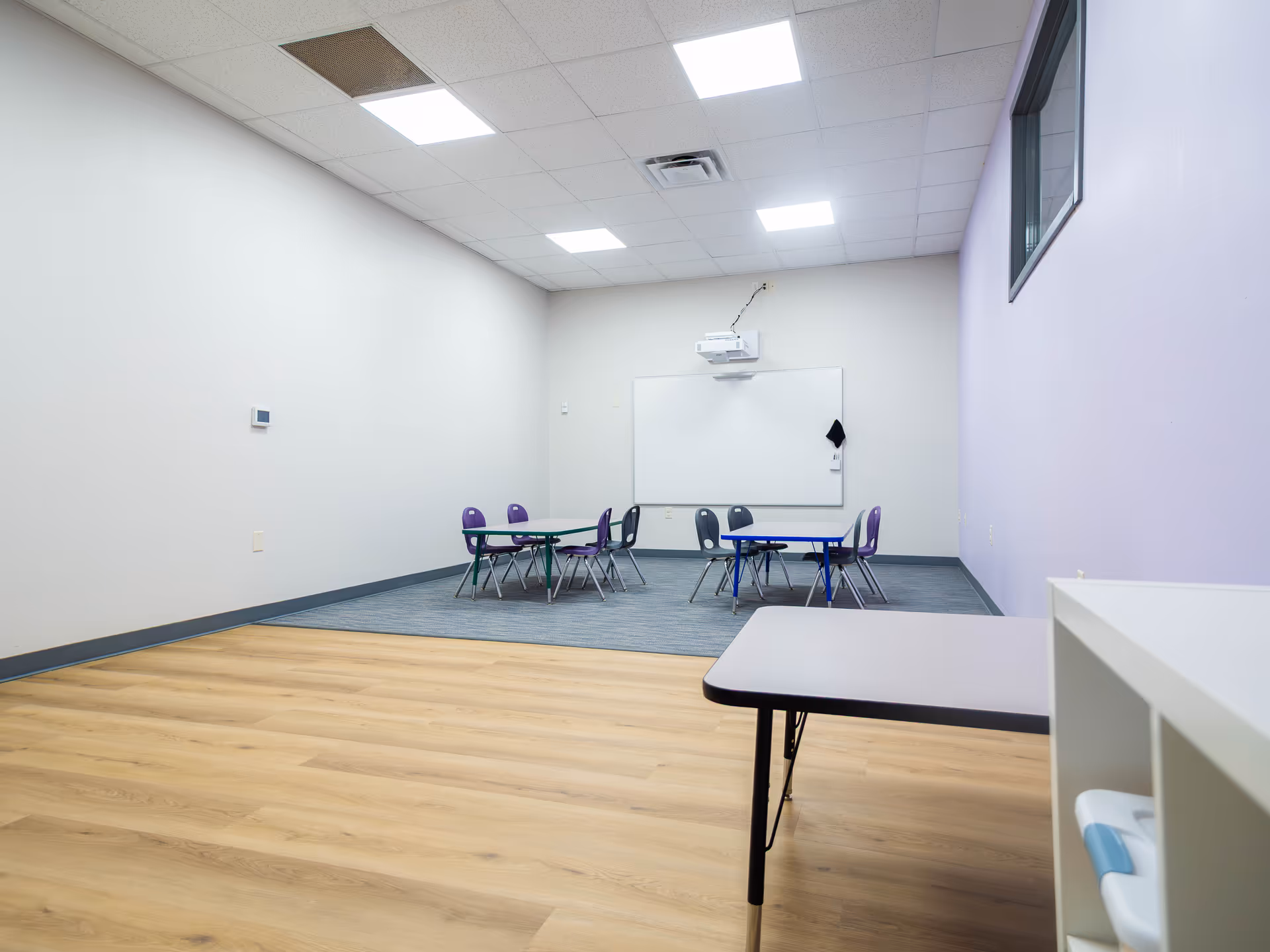 A classroom-style interior with small tables and purple chairs facing a whiteboard.
