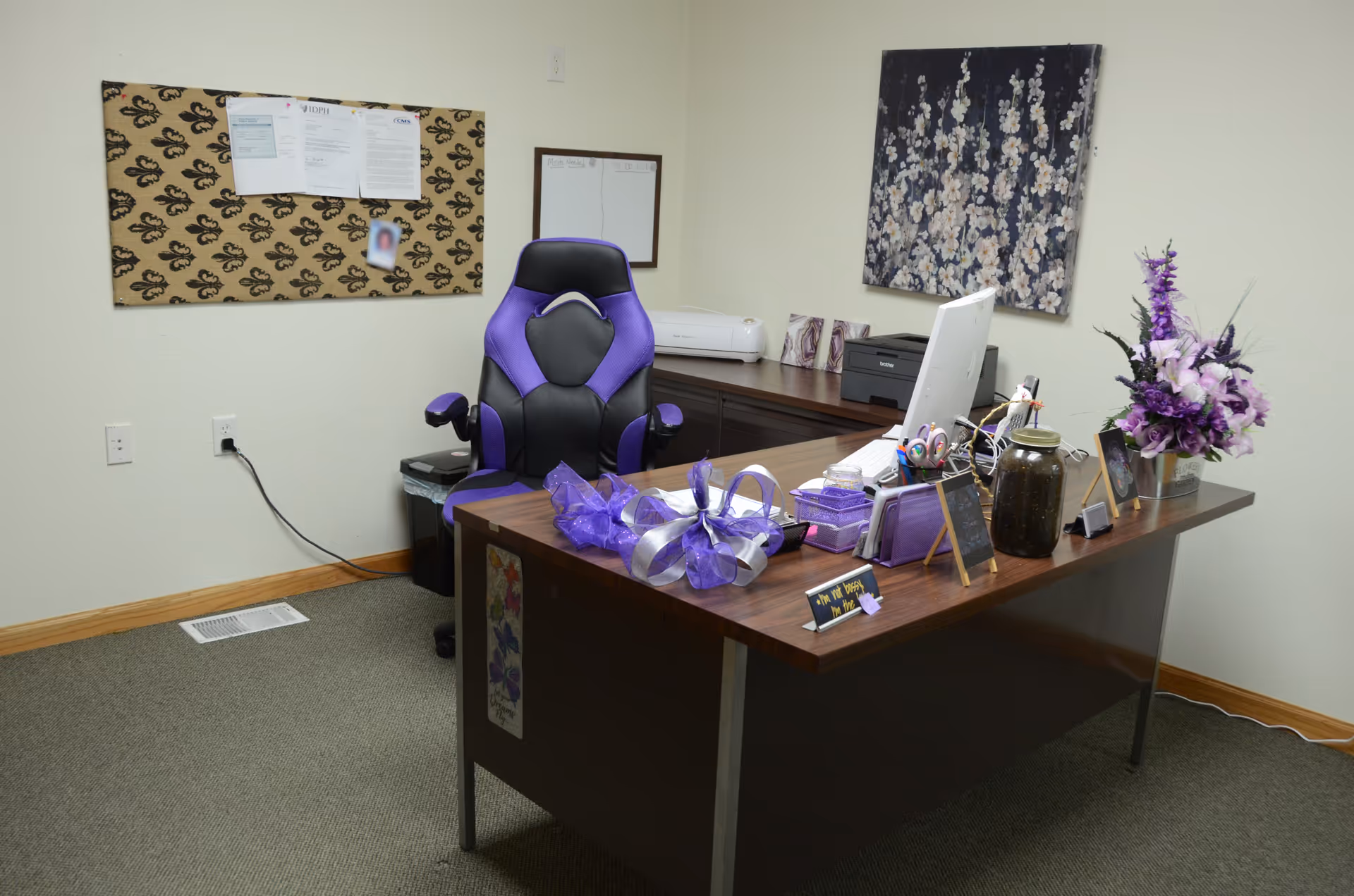 Office reception area with a purple chair, desk, computer, and decorative flowers.