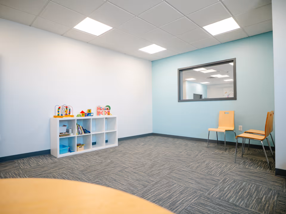 Bright play area with toy shelf, two chairs, and a windowed wall in a blue room