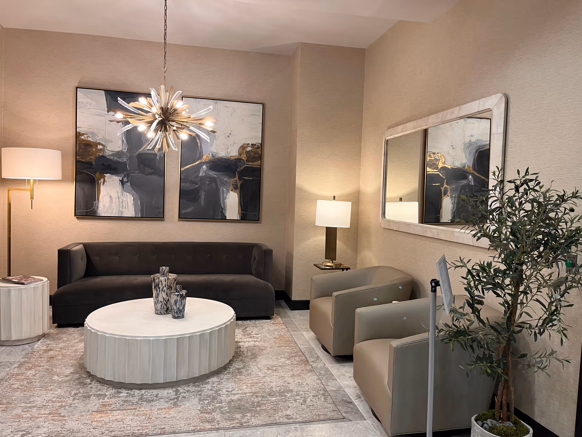 Modern living room lobby with beige walls, gray sofa, chairs, coffee table, and art.