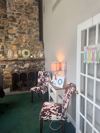 Cozy lounge with a stone fireplace, cowhide-pattern chairs, and a welcome sign.