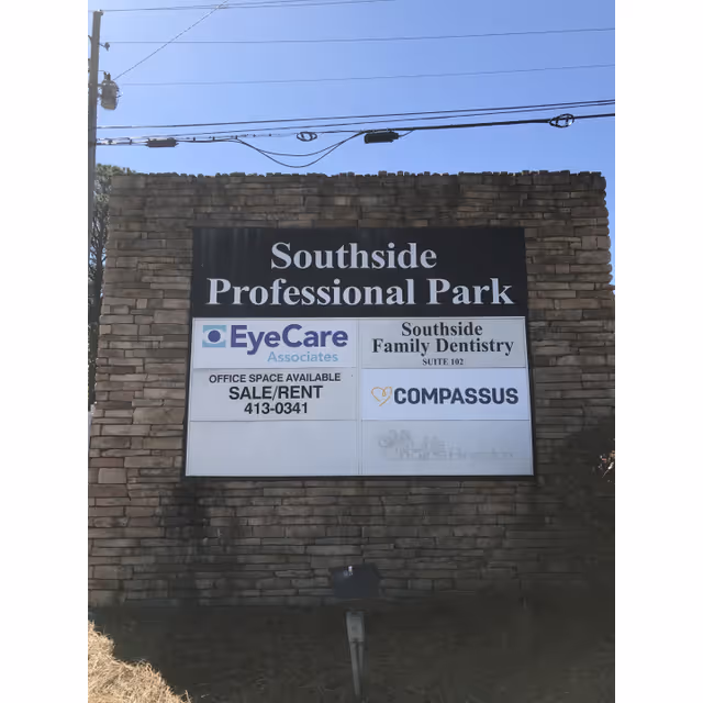 Outdoor brick sign wall displaying Compassus alongside EyeCare and family dentistry signs.