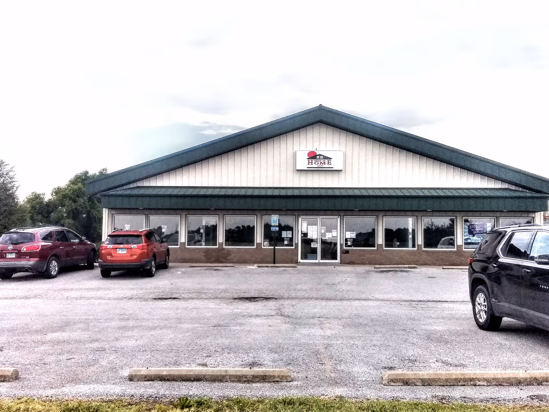 Front view of a Help at Home facility, a single-story building with cars parked in front.