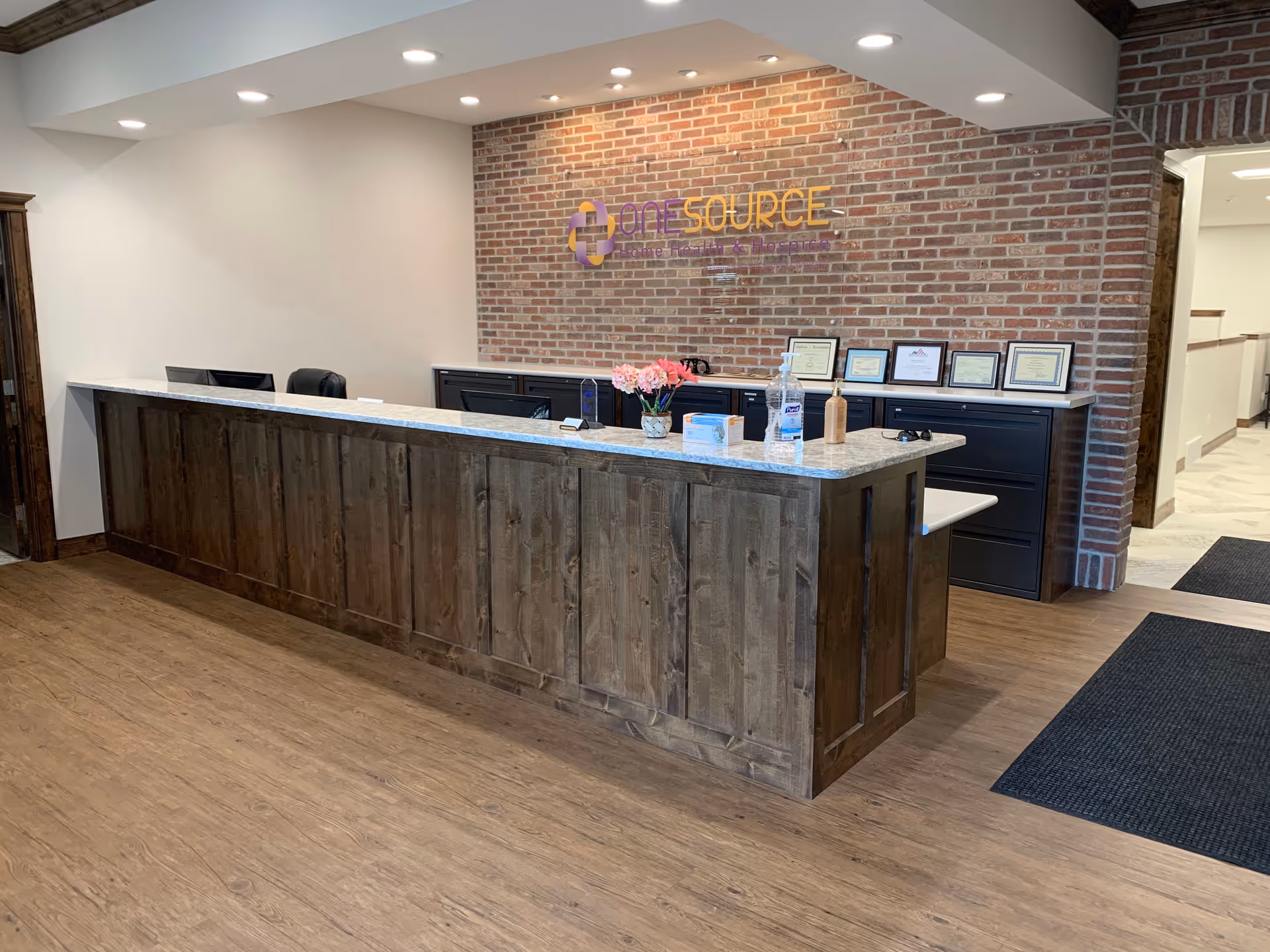 Reception desk in a brick-walled lobby with OneSource signage and certificates.