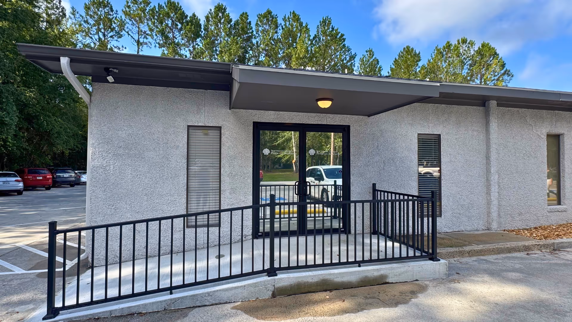 Exterior view of a small clinic entrance with glass doors, ramp, and metal railing.
