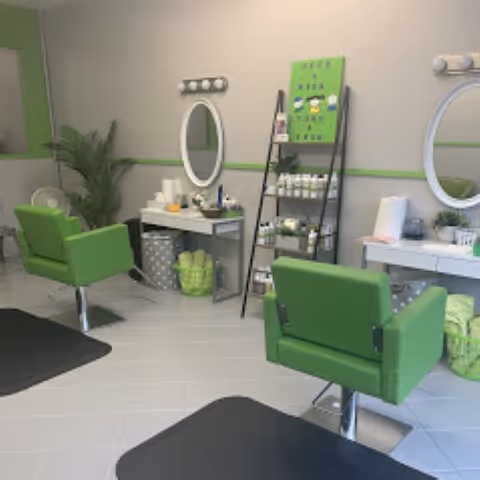 Interior of a bright salon area with green chairs, mirrors, and shelves.