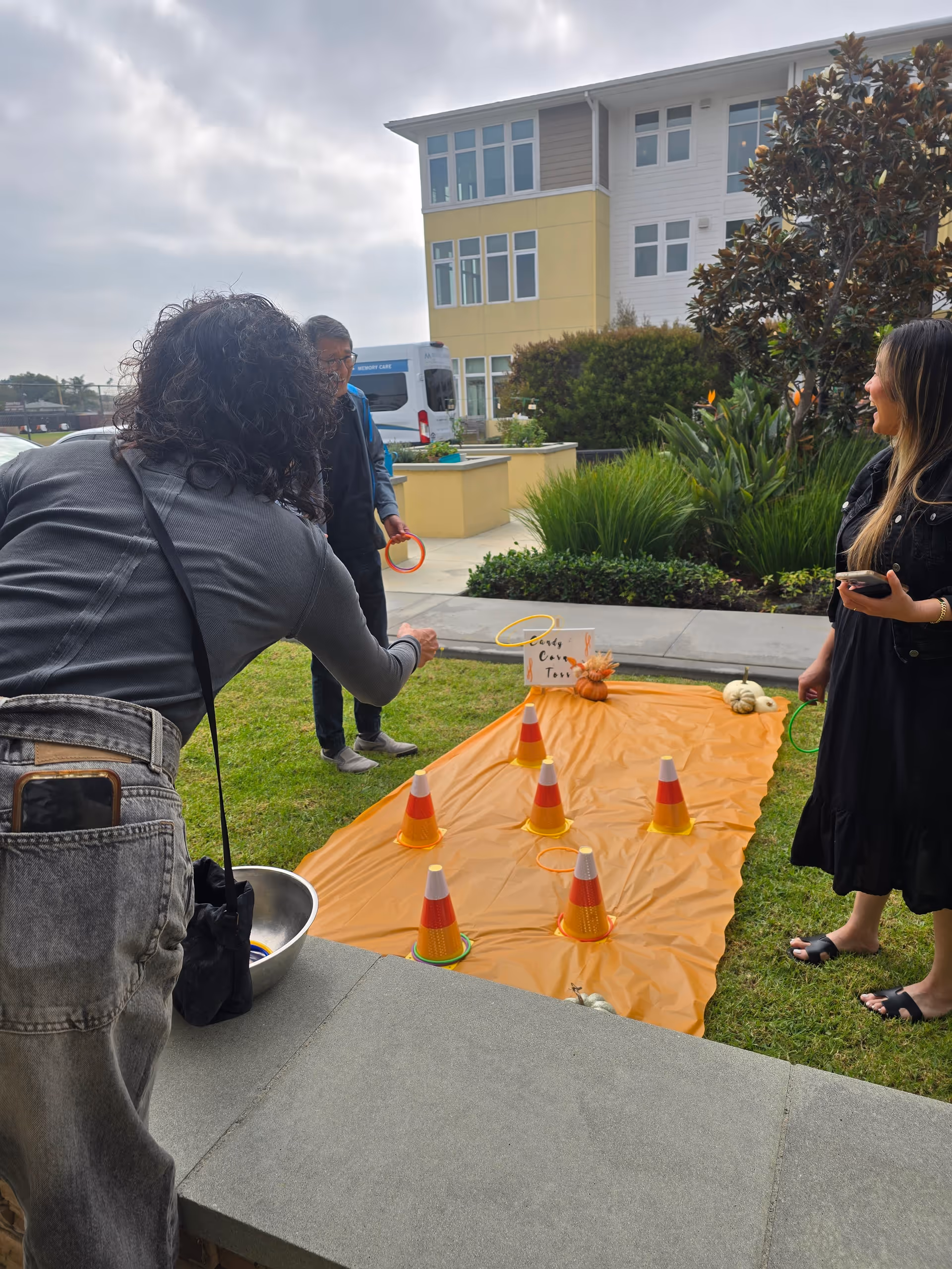 Outdoor scene at St Jude Cares with people playing ring-toss on an orange tarp.